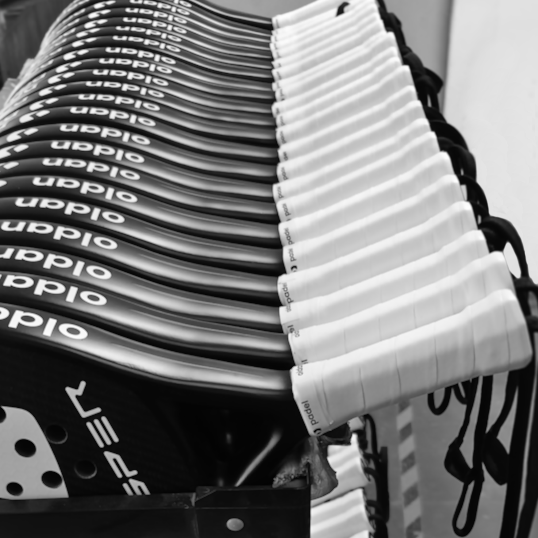 Stack of padel rackets with white grips and visible brand name on a black background. Paddle rackets in a line.