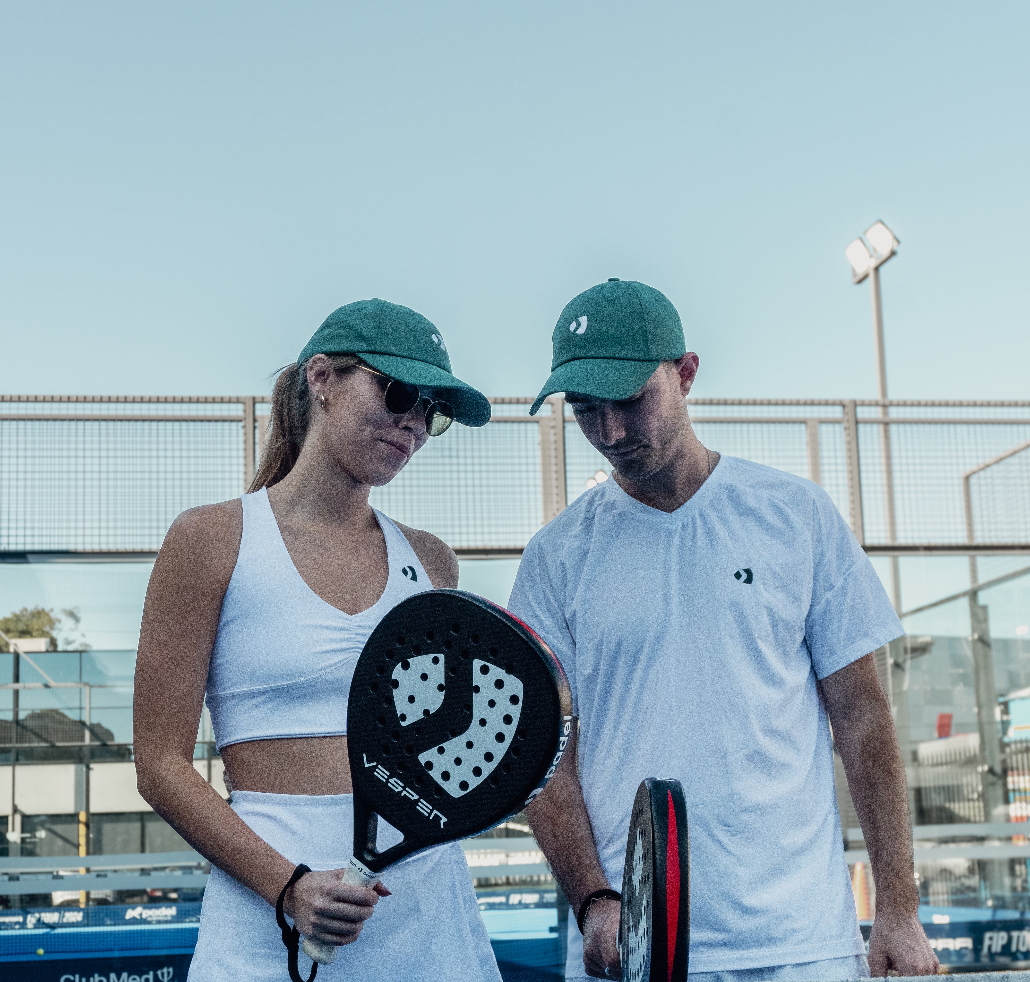 Two people on a tennis court holding paddle sports equipment. The padel racket is being held on a padel court. paddle players in the sun. Two Paddle Players. Wearing padel clothing and padle racquets. Two premium padel rackets. 